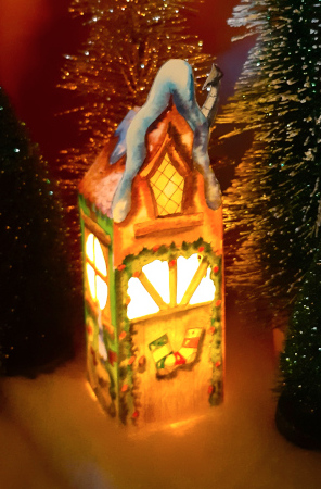 Une maison de Noël en papier en 3D, illustrée à l'aquarelle avec une bougie à l'intérieur.